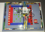 Foto eines Mühle spielenden Lego-Roboters auf einem speziell farbig markiertem, schematischen Mühlespielfeld